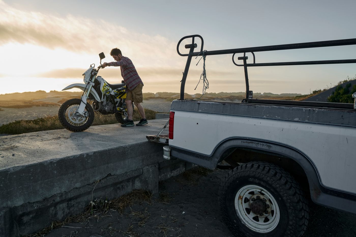 Hombre bajando una moto de la parte trasera de una camioneta al atardecer